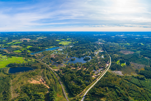Aerial view of a landscape featuring lush green forests winding roads and serene lakes under a clear blue sky Latvia. Aerial view of a landscape featuring lush green forests winding roads and serene lakes under a clear blue sky Latvia.