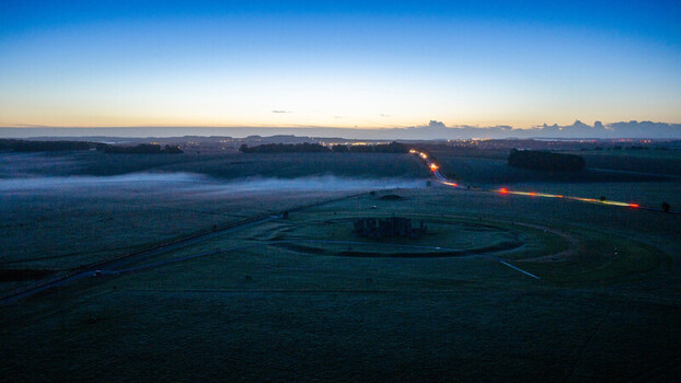 Aerial view of Stonehenge surrounded by mist in the early morning light with light trails from cars on the road in Salisbury England United Kingdom. Aerial view of Stonehenge surrounded by mist in the early morning light with light trails from cars on the road in Salisbury England United Kingdom.