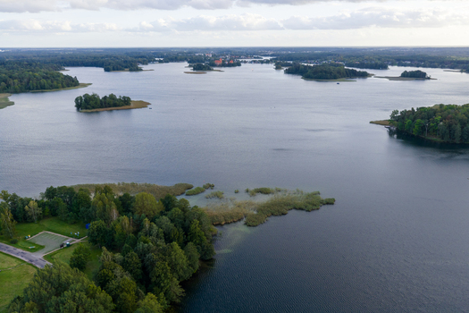 Aerial view of Galve Lake with lush green islands and the distant Trakai Island Castle under a cloudy sky in Lithuania. Aerial view of Galve Lake with lush green islands and the distant Trakai Island Castle under a cloudy sky in Lithuania.