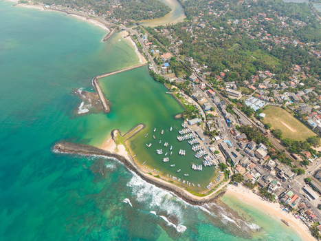 Aerial view of the coastal harbor with numerous fishing boats moored in turquoise waters along the lush shoreline in Hikkaduwa Southern Province Sri Lanka. Aerial view of the coastal harbor with numerous fishing boats moored in turquoise waters along the lush shoreline in Hikkaduwa Southern Province Sri Lanka.