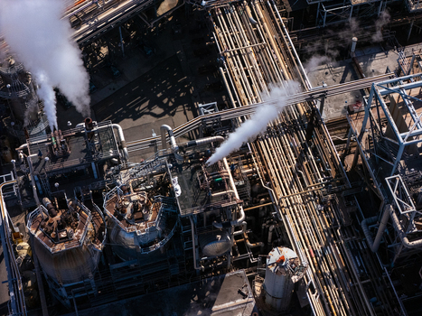 Aerial view of an industrial oil refinery featuring complex networks of metal pipes large storage tanks and steam rising from processing units in Carson California United States.