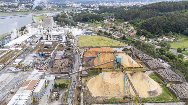 Aerial view of Biofabrica de Ence with large wood chip piles industrial structures and smoking chimneys near lush green hills Pontevedra Pontevedra Spain. Aerial view of Biofabrica de Ence with large wood chip piles industrial structures and smoking chimneys near lush green hills Pontevedra Pontevedra Spain.