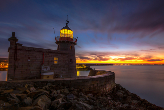 View of the historic stone Howth Lighthouse at Howth Harbour at sunset with a glowing lantern and clouds over the sea Ireland. View of the historic stone Howth Lighthouse at Howth Harbour at sunset with a glowing lantern and clouds over the sea Ireland.