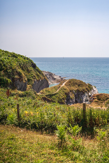 View of the rugged coastline at Lansallos beach with a winding coastal path grassy cliffs and the blue sea under a clear sky in Lansallos England United Kingdom. View of the rugged coastline at Lansallos beach with a winding coastal path grassy cliffs and the blue sea under a clear sky in Lansallos England United Kingdom.
