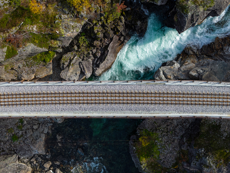 Aerial view of a railway bridge crossing a rocky river with turquoise water and autumn foliage in Bjorli Innlandet Norway. Aerial view of a railway bridge crossing a rocky river with turquoise water and autumn foliage in Bjorli Innlandet Norway.
