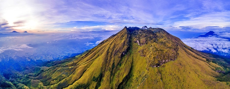 Aerial view of Mount Sumbing with its steep green slopes and rocky peak above a sea of clouds during sunrise in Temanggung Central Java Indonesia. Aerial view of Mount Sumbing with its steep green slopes and rocky peak above a sea of clouds during sunrise in Temanggung Central Java Indonesia.