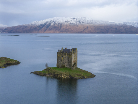 Aerial view of Castle Stalker on a small island in Loch Laich with snow capped mountains in the background Appin Scotland United Kingdom. Aerial view of Castle Stalker on a small island in Loch Laich with snow capped mountains in the background Appin Scotland United Kingdom.
