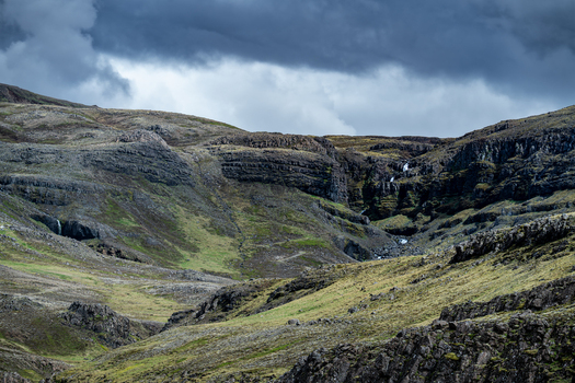 View of the rugged rocky cliffs and green mossy slopes of Hvalfjordur with small waterfalls under a dramatic cloudy sky Iceland. View of the rugged rocky cliffs and green mossy slopes of Hvalfjordur with small waterfalls under a dramatic cloudy sky Iceland.