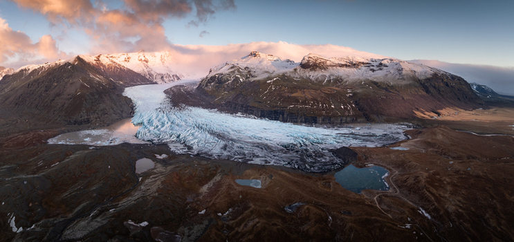 Aerial view of Svinafellsjokull glacier with icy blue crevasses rugged snow capped mountains dark volcanic terrain and glacial lagoons in Sveitarfelagid Hornafjordur Iceland. Aerial view of Svinafellsjokull glacier with icy blue crevasses rugged snow capped mountains dark volcanic terrain and glacial lagoons in Sveitarfelagid Hornafjordur Iceland.