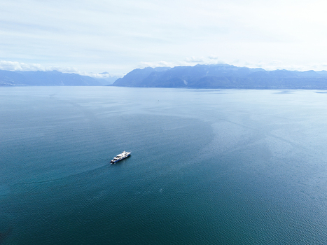 Aerial view of a ferry boat crossing the calm blue waters of Lake Geneva near the Ouchy Olympique waterfront with distant mountains in Lausanne Vaud Switzerland.