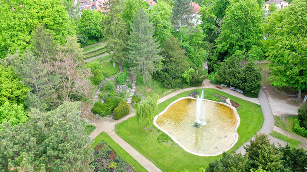 Aerial view of the Stadtpark featuring a central fountain in a pond surrounded by walking paths and lush green trees in Forchheim Bayern Germany. Aerial view of the Stadtpark featuring a central fountain in a pond surrounded by walking paths and lush green trees in Forchheim Bayern Germany.