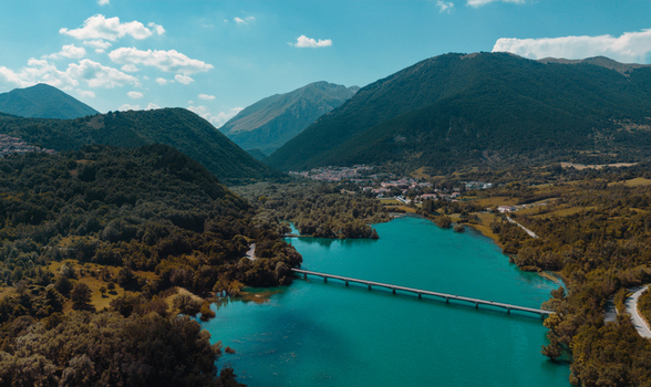 Aerial view of Lago di Barrea with its turquoise waters crossed by a bridge surrounded by lush green mountains and forests under a clear blue sky Province of L Aquila Abruzzo Italy.
