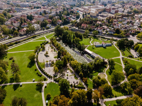 Aerial view of Tivoli Park featuring lush green lawns winding walking paths a central pond and surrounding urban architecture in Ljubljana Slovenia.