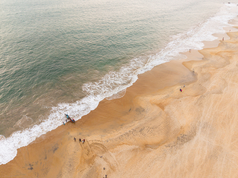 Aerial view of a sandy beach with turquoise ocean waves people walking along the shore and a small boat at the water s edge in Galle Southern Province Sri Lanka.