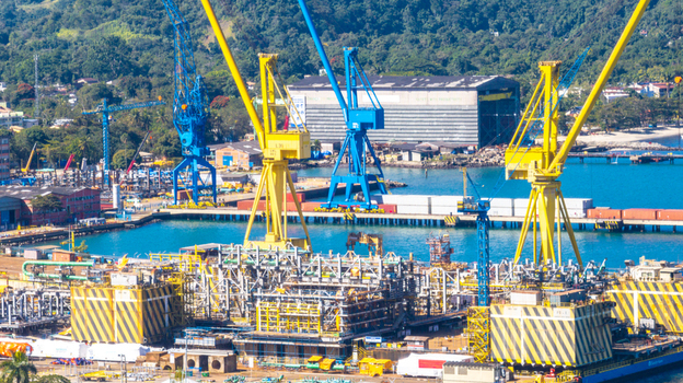 Aerial view of a busy industrial shipyard with large yellow and blue cranes metal structures and shipping containers along the waterfront in Angra dos Reis Rio de Janeiro Brazil.