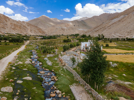Aerial view of a mountain stream flowing through the arid landscape of Ladakh with agricultural fields a small white house and rocky terrain in Ladakh Ladakh India. Aerial view of a mountain stream flowing through the arid landscape of Ladakh with agricultural fields a small white house and rocky terrain in Ladakh Ladakh India.