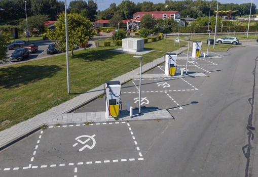 Aerial view of Shell Recharge charging station with multiple electric vehicle charging stalls in a parking lot surrounded by green grass and trees in Lelystad Flevoland Netherlands. Aerial view of Shell Recharge charging station with multiple electric vehicle charging stalls in a parking lot surrounded by green grass and trees in Lelystad Flevoland Netherlands.