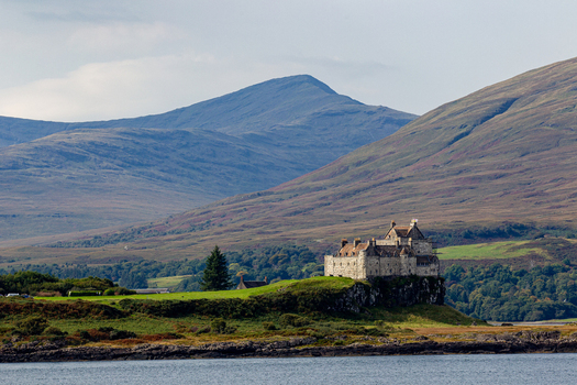 View of Duart Castle standing on a rocky cliff overlooking the sea with rolling mountains in the background in Isle of Mull Scotland United Kingdom.