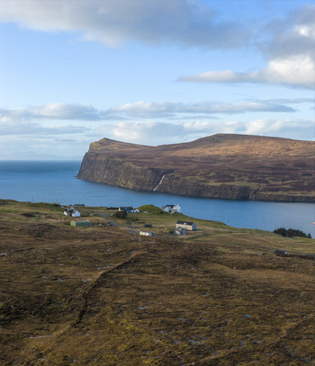 Aerial view of the rugged coastal landscape of Milovaig with steep cliffs overlooking the blue sea and scattered houses on the moorland in Milovaig Scotland United Kingdom.