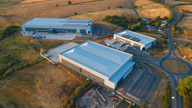 Aerial view of industrial warehouses surrounded by fields and a roundabout under sunset golden light in Wellingborough England United Kingdom. Aerial view of industrial warehouses surrounded by fields and a roundabout under sunset golden light in Wellingborough England United Kingdom.