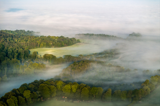 Aerial view of rolling green hills and dense woodlands partially covered by thick morning mist under a soft light Nuffield Oxfordshire United Kingdom. Aerial view of rolling green hills and dense woodlands partially covered by thick morning mist under a soft light Nuffield Oxfordshire United Kingdom.