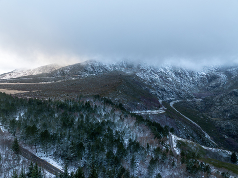 Aerial view of Serra da Estrela mountains covered in snow with a winding road and pine forest under a cloudy sky in Unhais da Serra Castelo Branco District Portugal. Aerial view of Serra da Estrela mountains covered in snow with a winding road and pine forest under a cloudy sky in Unhais da Serra Castelo Branco District Portugal.