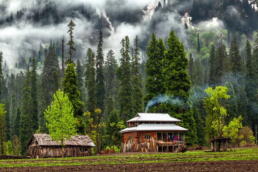View of a traditional wooden house with smoke rising from the chimney nestled among tall pine trees and misty mountains Arang Kel Azad Kashmir Pakistan. View of a traditional wooden house with smoke rising from the chimney nestled among tall pine trees and misty mountains Arang Kel Azad Kashmir Pakistan.