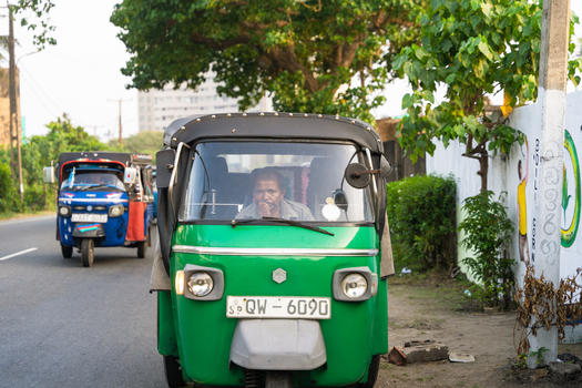Sri Lanka 21 January 2026 View of a green tuk tuk with a driver sitting inside on a roadside with lush green trees in the background.
