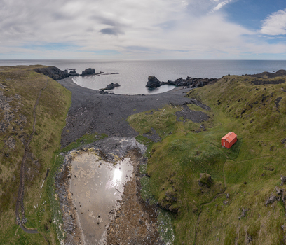 Aerial view of Djupalonssandur beach featuring a heart shaped pond a small red building on the grassy hillside and black volcanic sand along the rugged coastline Iceland. Aerial view of Djupalonssandur beach featuring a heart shaped pond a small red building on the grassy hillside and black volcanic sand along the rugged coastline Iceland.