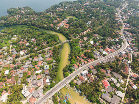 Aerial view of the lush tropical landscape and residential houses along the waterway with a bridge and winding road in Dodanduwa Southern Province Sri Lanka. Aerial view of the lush tropical landscape and residential houses along the waterway with a bridge and winding road in Dodanduwa Southern Province Sri Lanka.