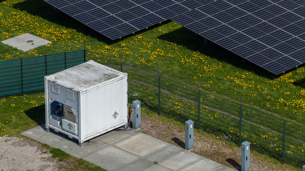 Aerial view of solar panels and a white energy storage container on a green field with yellow flowers Warmenhuizen North Holland Netherlands. Aerial view of solar panels and a white energy storage container on a green field with yellow flowers Warmenhuizen North Holland Netherlands.