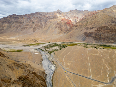 Aerial view of the rugged Zanskar valley landscape featuring a winding river a small bridge and a road cutting through the arid rocky terrain in Zanskar Ladakh India.