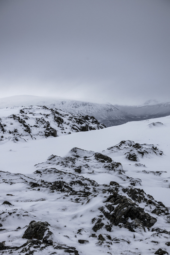 View of snowy mountain peaks and rocky terrain under a cloudy winter sky in Kvaloya Troms Norway.