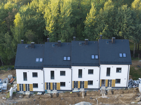 Aerial view of modern terraced houses with dark roofs and white facades under construction surrounded by lush green trees in Wieliczka Lesser Poland Voivode Poland.