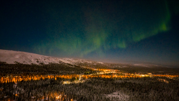 Aerial view of Luosto with the Aurora Borealis dancing over snow covered forests and the glowing lights of the resort at night Sodankyla Lapland Finland. Aerial view of Luosto with the Aurora Borealis dancing over snow covered forests and the glowing lights of the resort at night Sodankyla Lapland Finland.