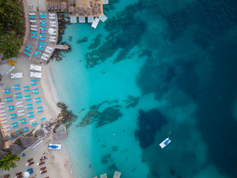 Aerial view of turquoise crystal clear water and a white sandy beach with blue sunbeds and umbrellas in Ksamil Vlore County Albania. Aerial view of turquoise crystal clear water and a white sandy beach with blue sunbeds and umbrellas in Ksamil Vlore County Albania.