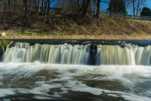 View of Ventas Rumba waterfall flowing over the limestone ledge with trees on the riverbank in Kuldiga Kuldigas novads Latvia. View of Ventas Rumba waterfall flowing over the limestone ledge with trees on the riverbank in Kuldiga Kuldigas novads Latvia.