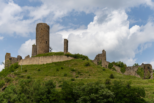 View of the historic Monreal Castle ruins with its prominent stone tower and crumbling walls on a green hill under a cloudy sky Monreal Rheinland Pfalz Germany. View of the historic Monreal Castle ruins with its prominent stone tower and crumbling walls on a green hill under a cloudy sky Monreal Rheinland Pfalz Germany.