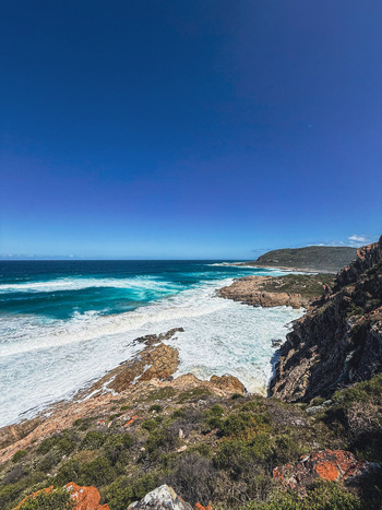 View of the rugged coastline with crashing waves against rocky cliffs and turquoise water under a clear blue sky in Plettenberg Bay Western Cape South Africa. View of the rugged coastline with crashing waves against rocky cliffs and turquoise water under a clear blue sky in Plettenberg Bay Western Cape South Africa.
