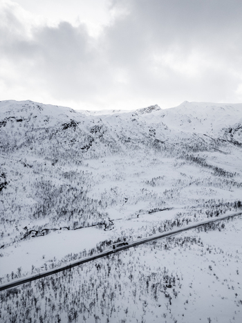 Aerial view of a winding road cutting through a vast snow covered mountain valley with sparse winter trees under a cloudy sky Ersfjord Troms Norway. Aerial view of a winding road cutting through a vast snow covered mountain valley with sparse winter trees under a cloudy sky Ersfjord Troms Norway.