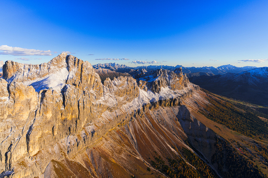 Aerial view of Catinaccio peaks dusted with snow casting long shadows over golden valleys under a clear blue sky Vigo di Fassa Trentino South Tyrol Italy.