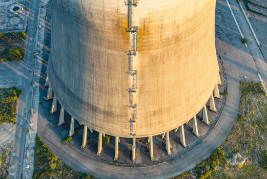 Aerial view of a massive concrete cooling tower at an industrial energy facility featuring external ladders and support columns in Trino Piedmont Italy.