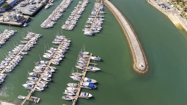 Aerial view of numerous sailboats and yachts docked in the marina with a stone breakwater extending into the calm green water in Zumaia Basque Country Spain.