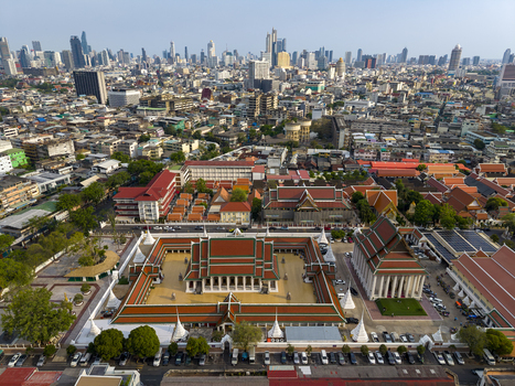 Bangkok Thailand 26 April 2026 Aerial view of a historic Buddhist temple complex with traditional red and green tiled roofs set against the modern city skyline and skyscrapers.