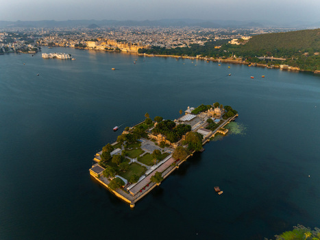 Aerial view of Jag Mandir palace on an island in Lake Pichola surrounded by calm water with the historic city of Udaipur in the background Udaipur Rajasthan India.