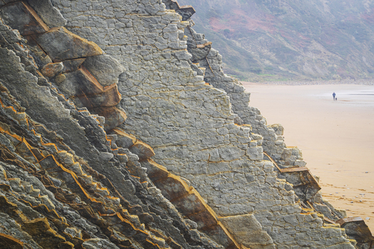 View of the unique flysch rock formations and a person walking on the sandy beach at Playa de Sopelana in Vizcaya Pais Vasco Spain. View of the unique flysch rock formations and a person walking on the sandy beach at Playa de Sopelana in Vizcaya Pais Vasco Spain.