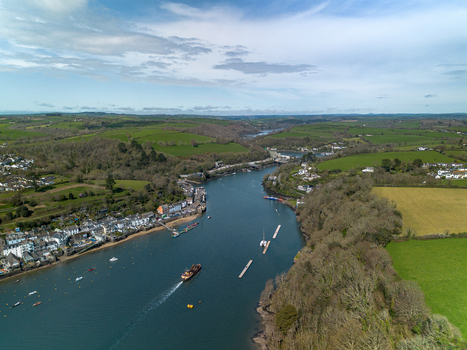 Aerial view of the Fowey river flowing past the historic town of Fowey with boats moored in the water and lush green countryside in Fowey Cornwall United Kingdom. Aerial view of the Fowey river flowing past the historic town of Fowey with boats moored in the water and lush green countryside in Fowey Cornwall United Kingdom.