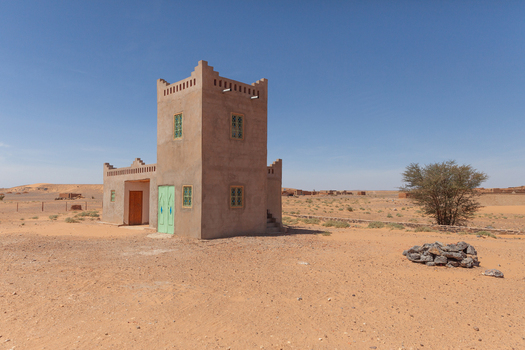 View of a traditional earthen adobe building standing in the arid desert landscape under a clear blue sky in Morocco.