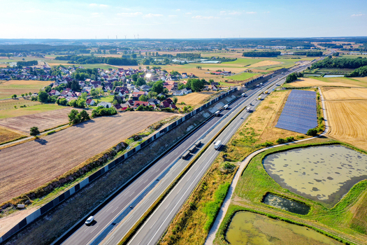 Nurnberg Germany 18 May 2024 Aerial view of the A73 highway with traffic noise barriers solar panels and a small village surrounded by green fields and ponds. Nurnberg Germany 18 May 2024 Aerial view of the A73 highway with traffic noise barriers solar panels and a small village surrounded by green fields and ponds.