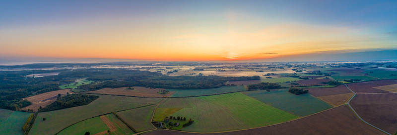 Aerial view of the agricultural landscape near Jelgava featuring vast green fields patches of forest and morning mist under a golden sunrise sky in Jelgava Latvia. Aerial view of the agricultural landscape near Jelgava featuring vast green fields patches of forest and morning mist under a golden sunrise sky in Jelgava Latvia.
